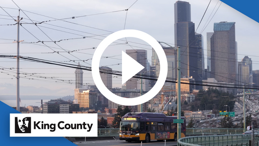 Downtown Seattle skyline with bus in foreground, large play button over image