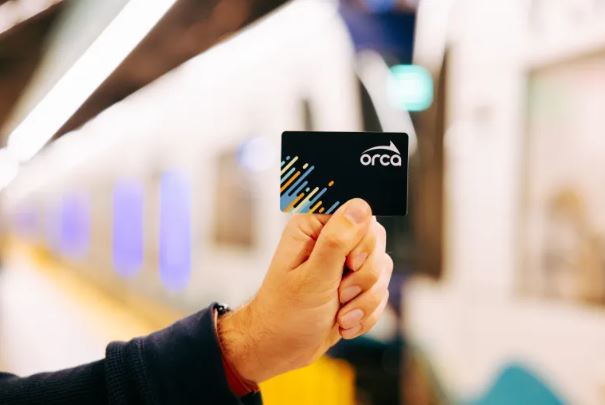 an in focus photo of a person holding a black new ORCA card with a blurry background image of the link light rail