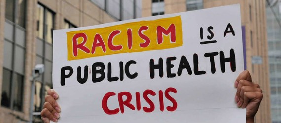 Hands holding sign that says Racism is a Public Health Crisis 