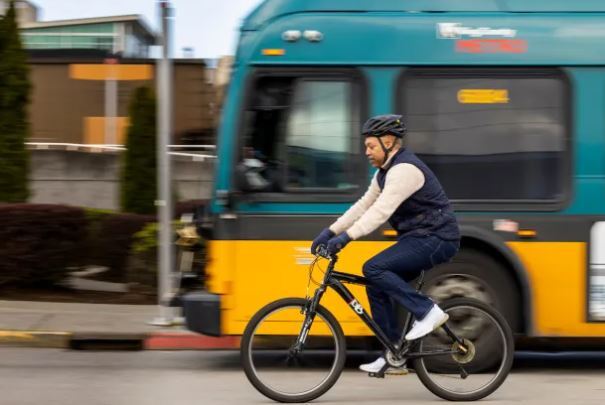 Image of a blurry bus and a man riding a bicycle with a helmet 