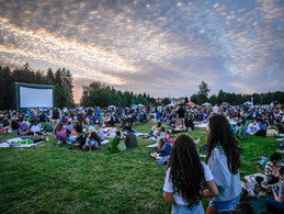 People lie and sit in front of a large outdoor screen at Marymoor Park.