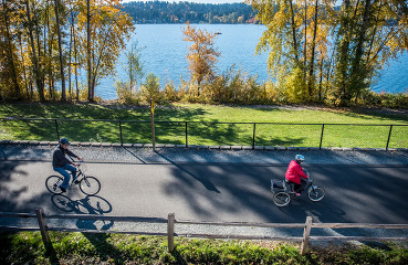 Two people ride bikes on the Eastlake Sammamish Trail, a paved trail with a view of the lake. 