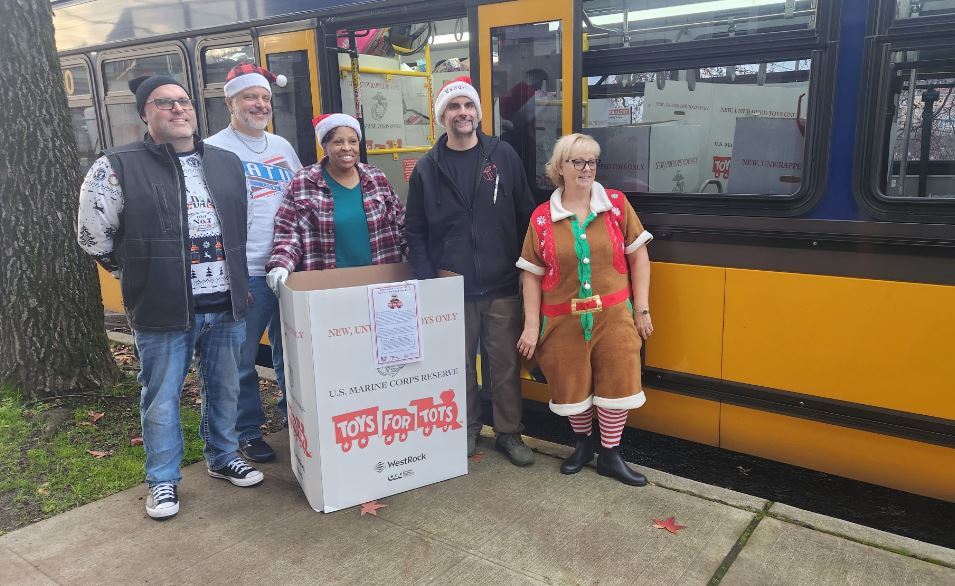 Picture of 5 metro employees with a Toys for Tots box and next to a Metro bus