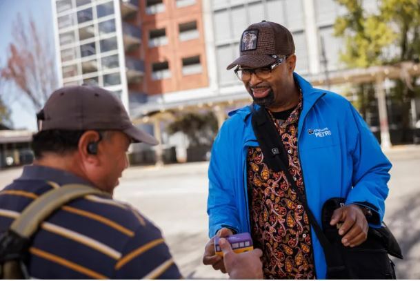 A Metro Ambassador in blue coat and hat interacts with a transit rider on April 27, 2023.