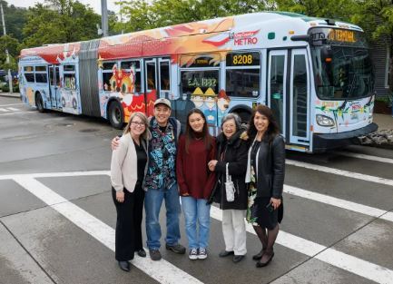 Picture shows group of Metro employees in front of Operator Sakado's art emblazoned across the sides of a 60-foot-long bus.