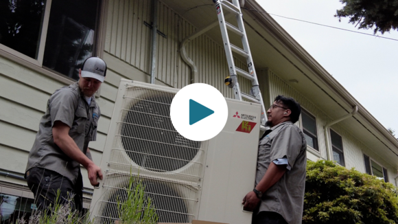 Contractors install a heat pump at a home in Skyway. A video play icon is overlayed over the photo.