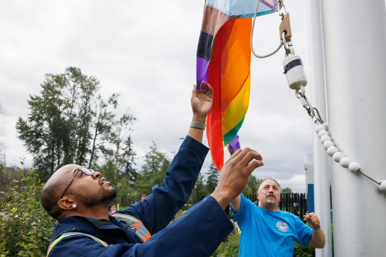 Image of two Metro employees raising the pride flag