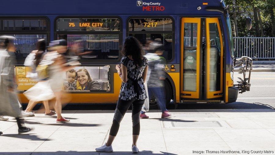 Image of route 75 bus with a rider waiting at the bus stop and blurry images of people walking by