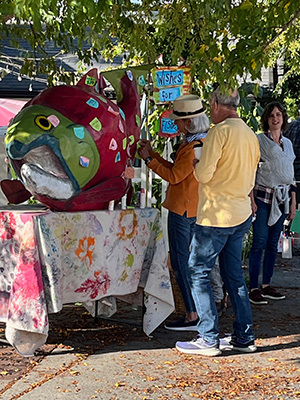 People walking at a fair and looking at a large paper mâché salmon fish