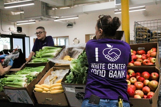 Volunteers at White Center Food Bank organizing fresh produce, including bananas, celery, and apples.