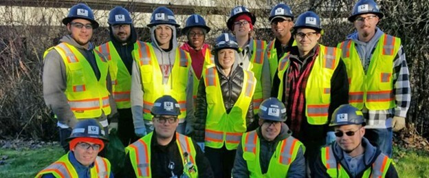 A group of people wearing hard hats and high visability vests grouped together posing for a photo. 