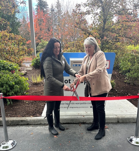 Elections Director Julie Wise and Councilmember Claudia Balducci cut a red ribbon in front of the new drop box at North Bellevue Community Center