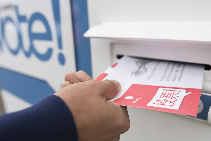 A photo of a hand putting a ballot in a secure King County ballot box