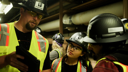 Three operators in training in personal protective equipment review information inside a treatment plant. 