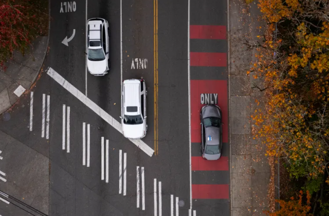 birds eye picture  of three cars. Two white cars are in the correct land and a dark car is in a red bus only lane