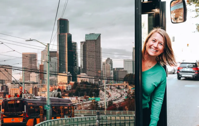 Picture of Michelle Alison leaning out of a bus the the city behind her