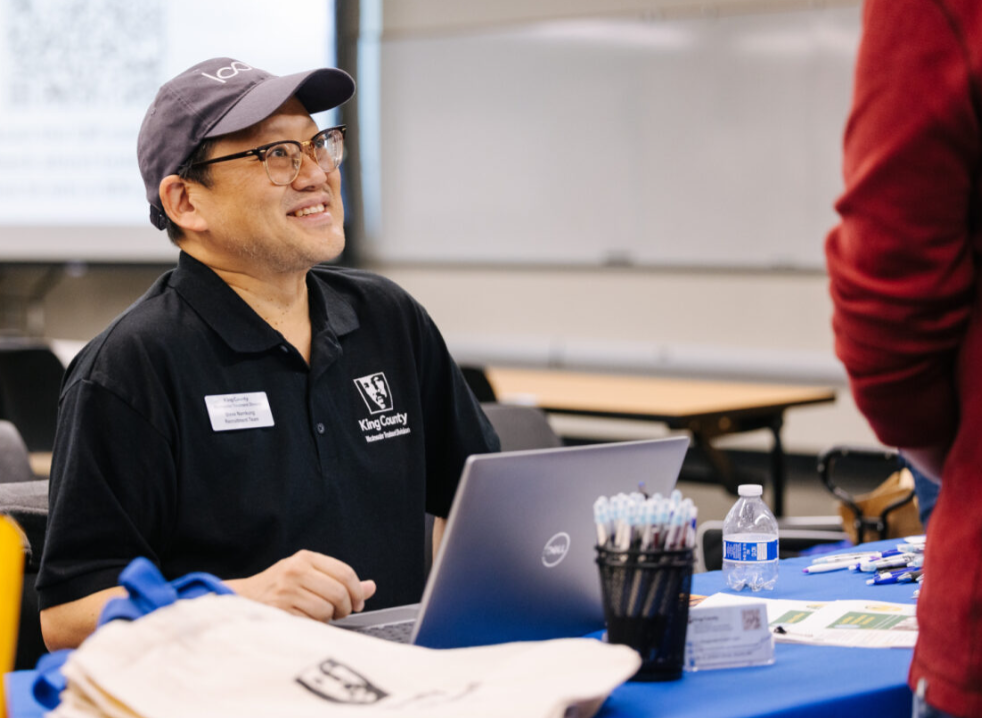 King County staff member sitting at a table and smiling at another person outside of the frame. 