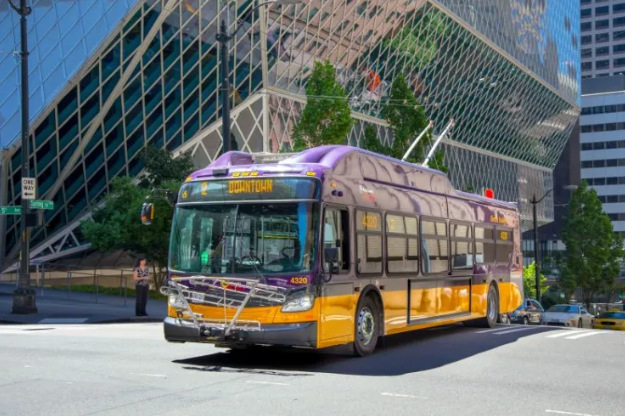 Image of route 2 bus, purple and gold driving in front of Seattle Central library connected to the trolley lines