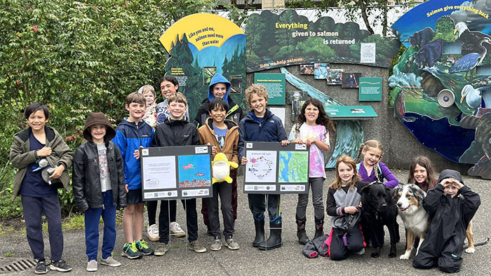 Group of kids standing outside holding drawings of salmon and a map of the Puget Sound