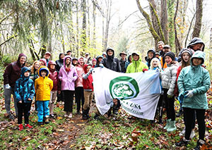 Group of people in a forest holding a banner with a picture of a tree on it
