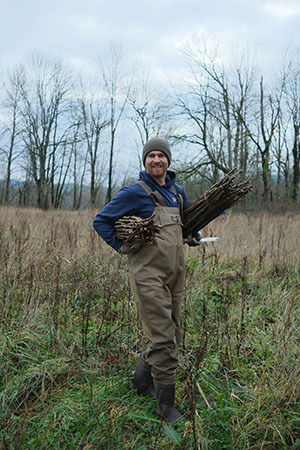 Photo showing a person carrying two bundles of sticks in a field