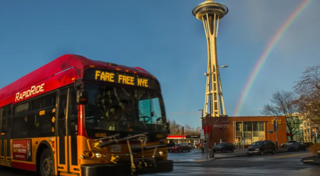 RapipdRide with sign that says 'Fare Free NYE" in front of Sspace Needle with a rainbow