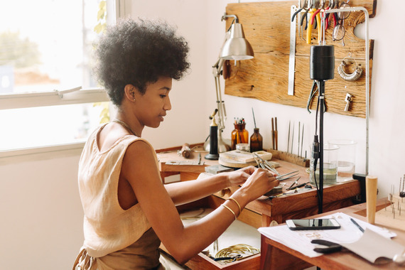 A Black woman makes jewelry at a bench
