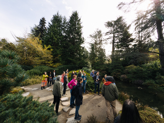 A group of people tours Kubota Garden, standing on a path surrounded by trees and greenery.