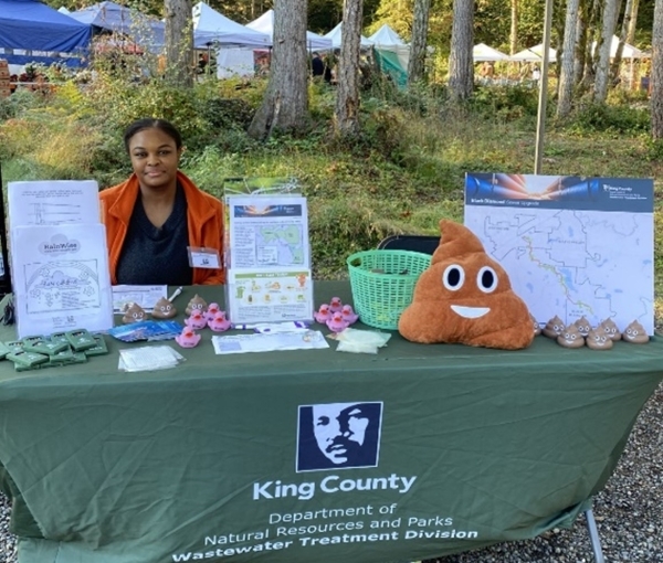 An outreach team member sits at a table with project information and giveaways. 