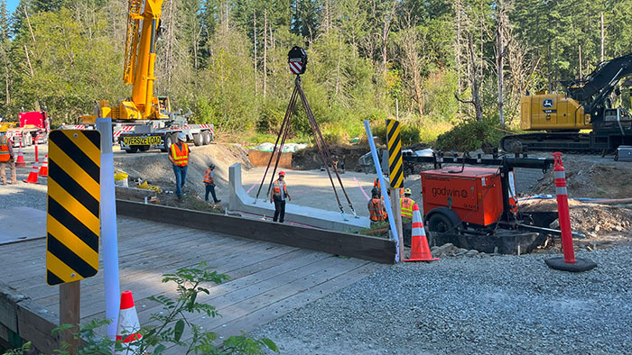 Crane and workers on the ground installing a concrete box culvert beside a bridge