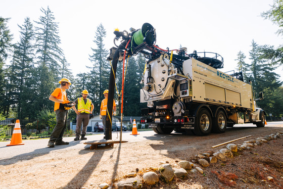 Crew members stand beside a large pipe-cleaning truck with hoses extended.