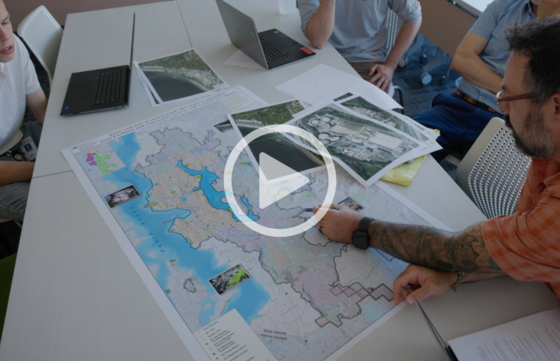 People sit around a table reviewing a large map of King County with aerial photos spread out.