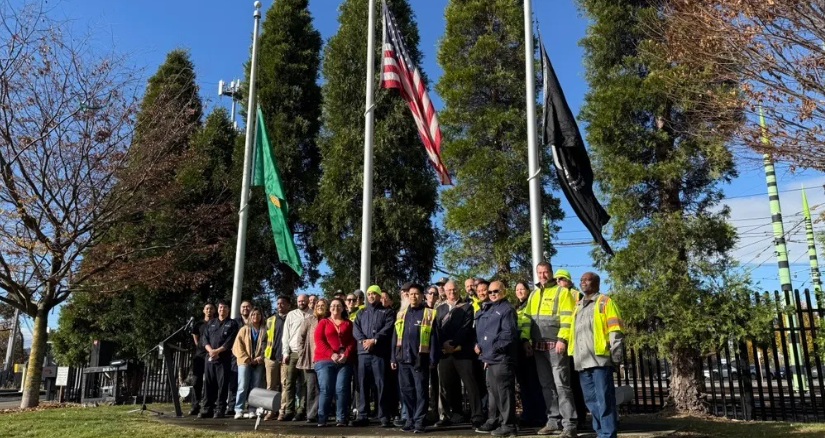 Image of a large group of employees under flag poles of the America, Washington and POW flags