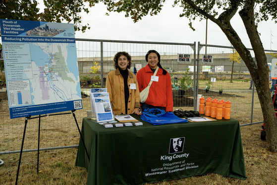 Two people stand in a park near a table and project materials