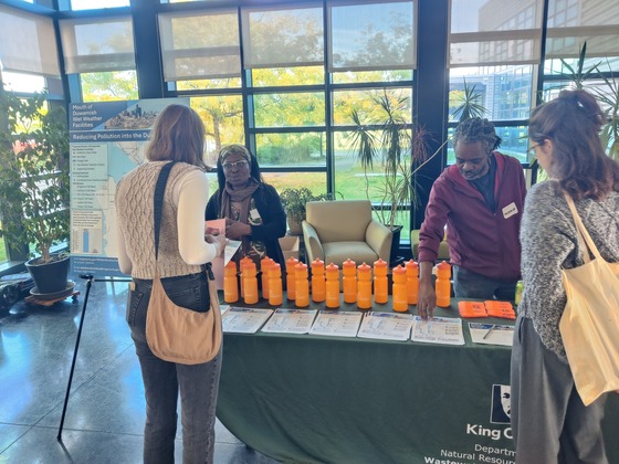 Four people stand talking around a table with water bottle giveaways and project materials.