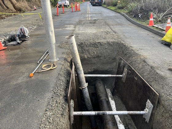 The exposed water force main in the middle of Discovery Park Boulevard with shoring in the trench and construction vehicles in the background