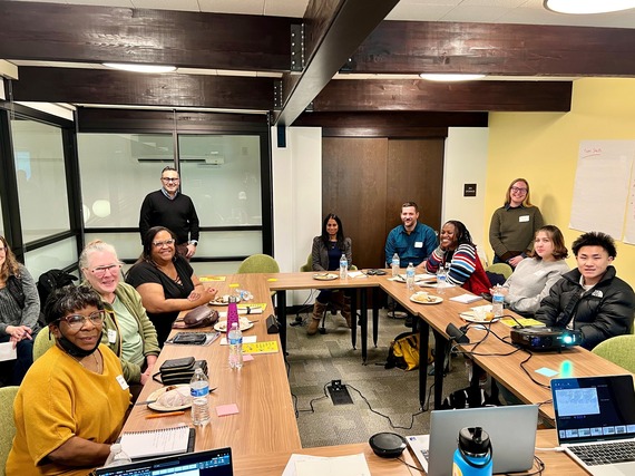 A group of people sit around a conference table and are smiling at the camera