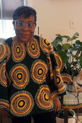 A Black woman smiles at the camera with a green plant in the background