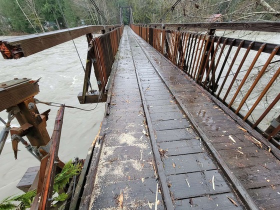 A wooden bridge over a river with a damaged railing