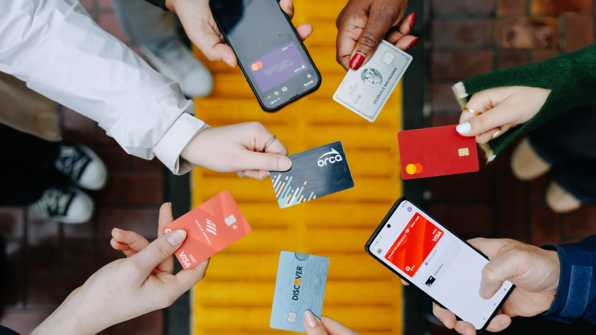 image of multiple hands holding debit cards, credit cards, Phone wallets and an ORCA card