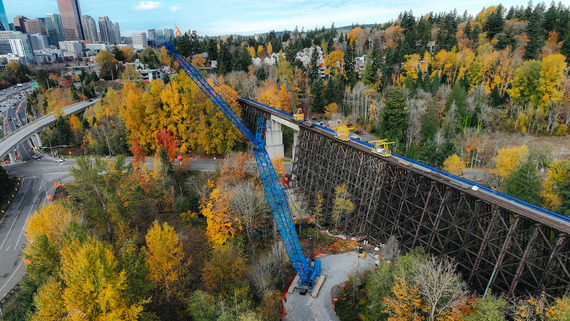 Aerial view of the Wilburton Trestle construction. Vibrant fall trees, a large wooden trestle, and cranes. 