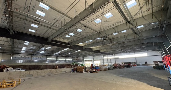 Interior of an industrial building showing a concrete floor and ceiling with skylighting. A variety of construction equipment sits along the edges.