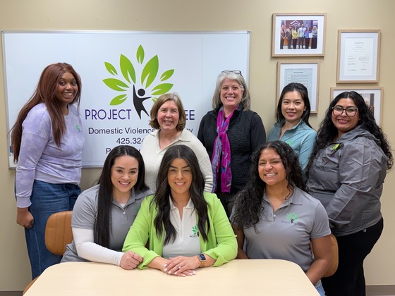 Councilmember Balducci and staff from Project Be Free stand in front of the logo of a person jumping surrounded by green leaves