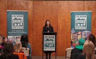 Councilmember Fain standing in front of a podium with two banners saying low income housing institute