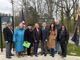 Councilmember Fain standing with several individuals in front of a new sign by a road with trees in the background