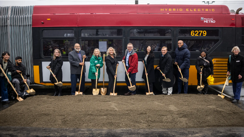 Image of twelve people with a shovel breaking ground in front of RapidRide bus