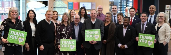 A group of people stand together holding signs that say "THANK YOU" with a heart design on them.
