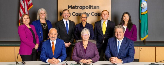 The nine members of the King County Council posing on the council dias in the King County Council chambers.
