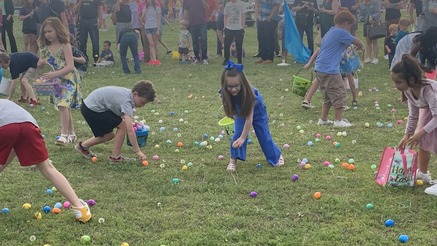 A group of children pick up easter eggs on grass.
