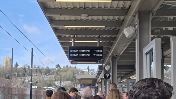 A crowd of people on a light rail train platform, above an electronic board reads "Downtown Redmond, 1 min."